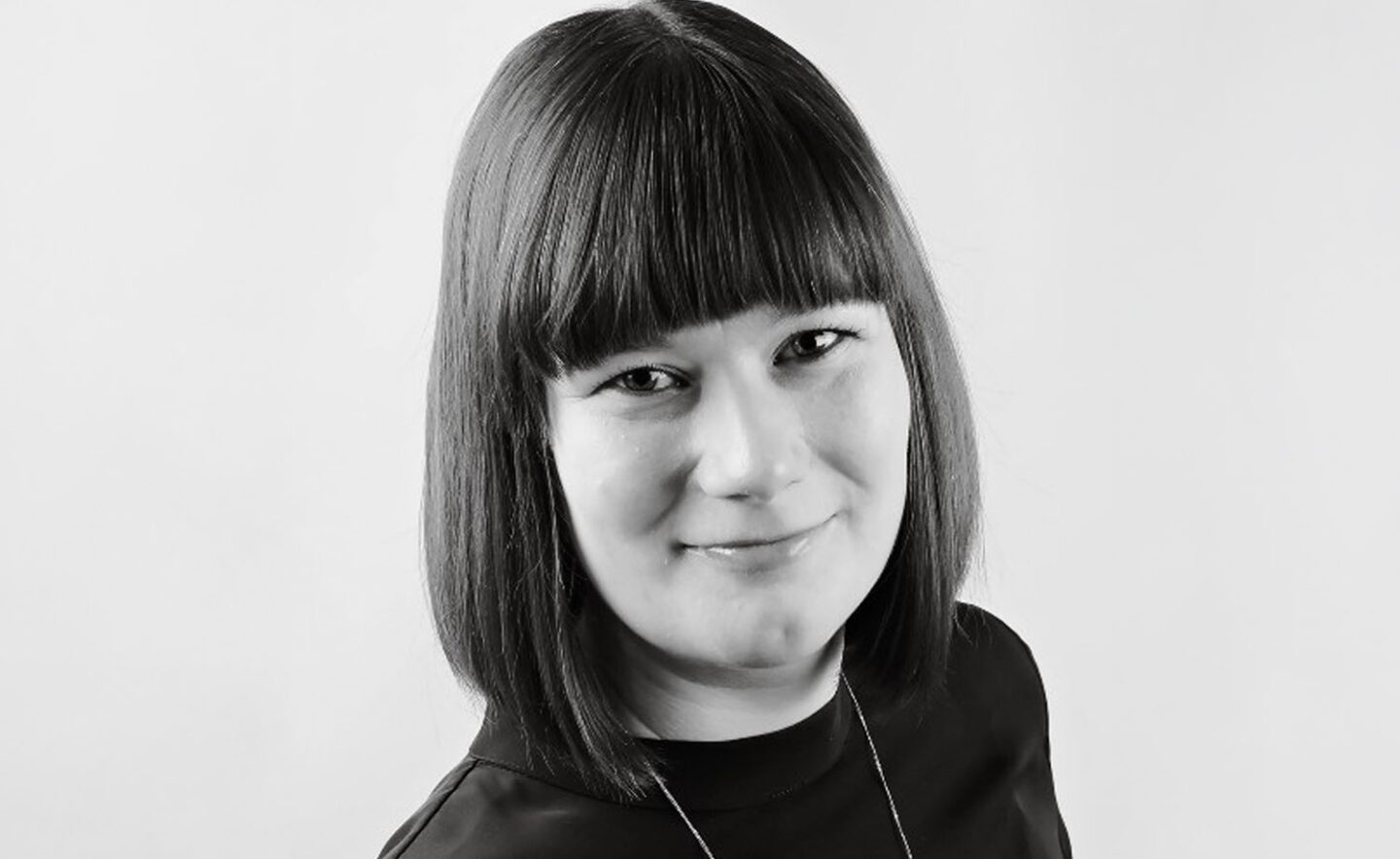 Headshot of Carly Jones; a black and white photograph of a white woman with dark hair wearing a black top.