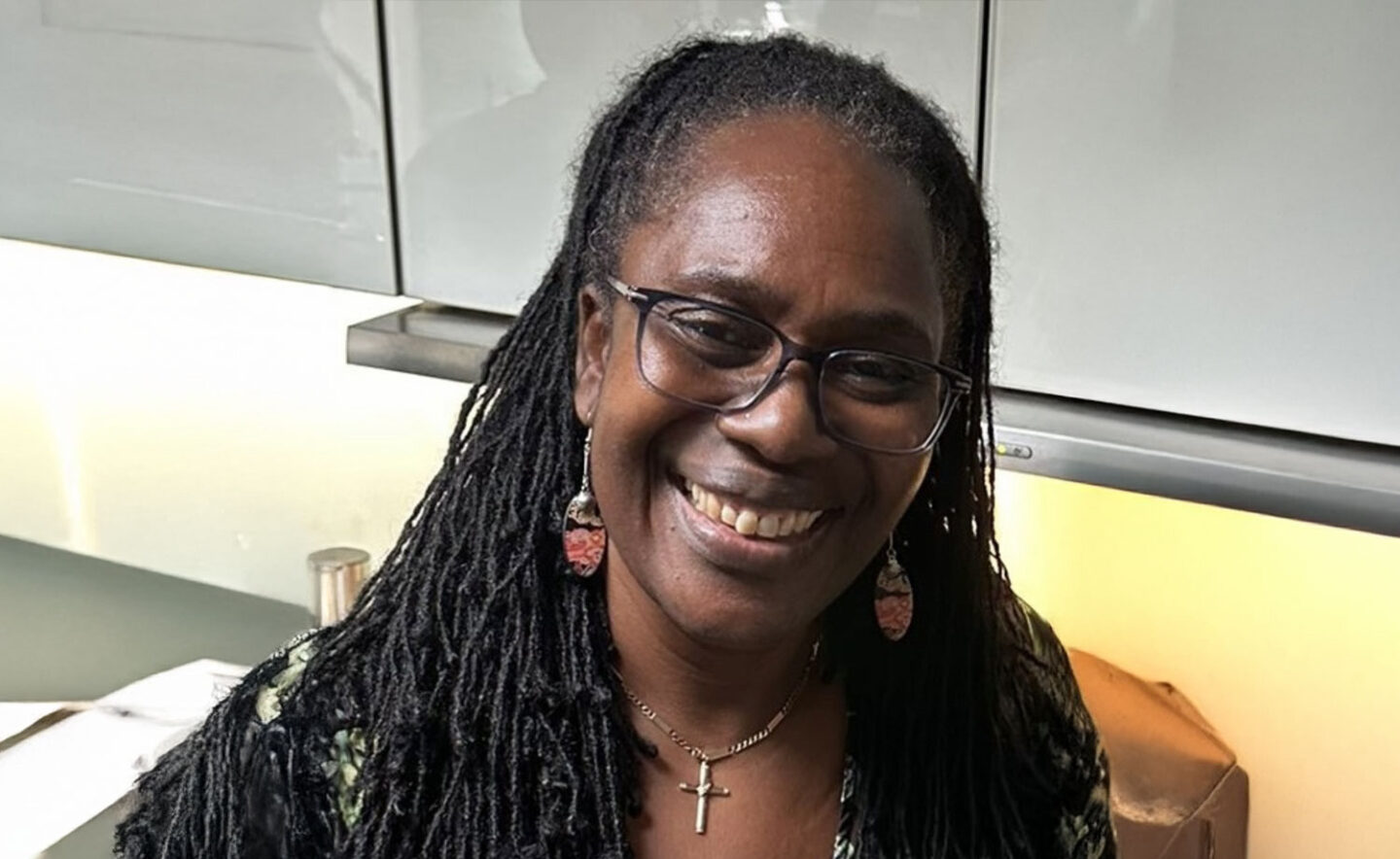 Headshot of Elaine Barrett - a Black woman with long braided hair, wearing glasses, earrings, and a cross necklace.