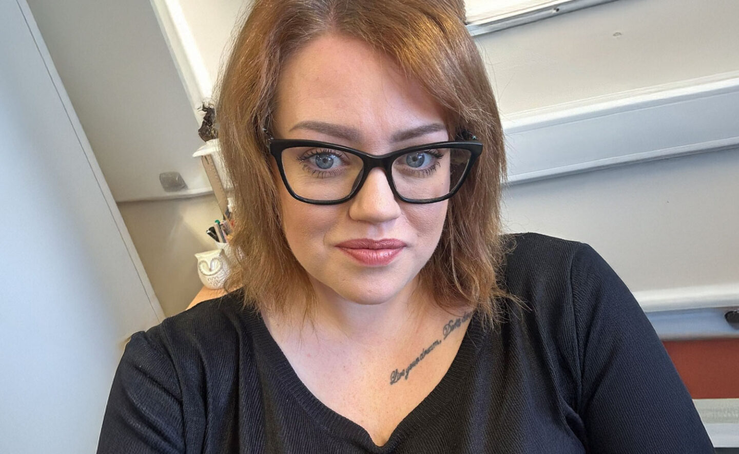 Headshot of Louise Bourne - a white woman with shoulder-length brown hair and glasses, wearing a black top with a tattoo visible on her collarbone.