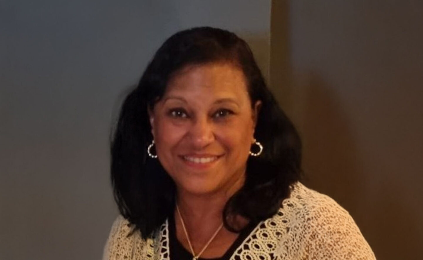 Headshot of Yvette John - a smiling woman with black hair, wearing a black top and a light-coloured cardigan.