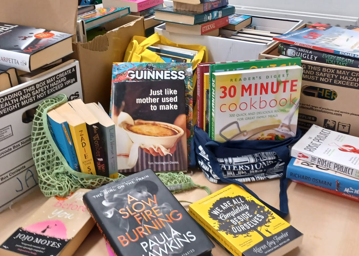 A collection of books stacked and scattered on a table, including cookbooks, novels, and non-fiction.