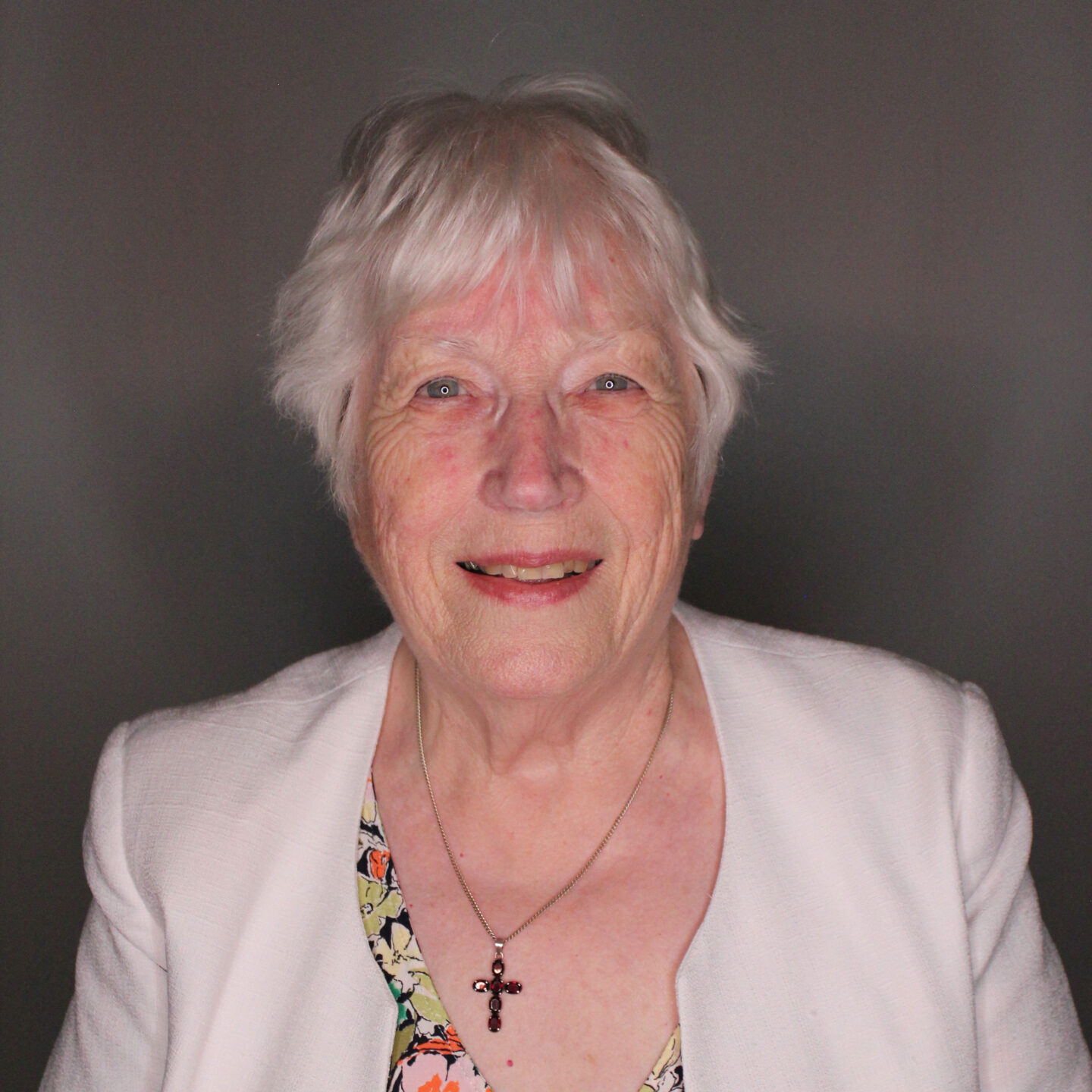 Headshot of Dr Christine Parkinson - a smiling woman with white hair, wearing a white jacket and a cross necklace.