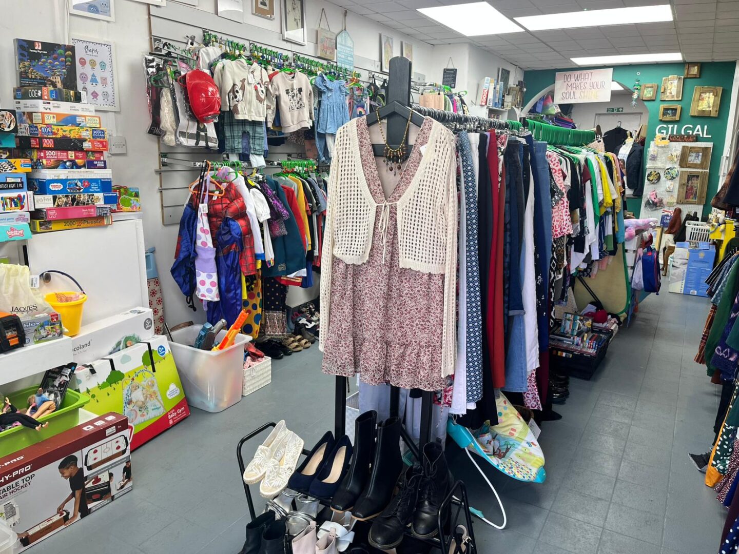 A colorful thrift store interior featuring racks of clothing, shoes, and various toys. The space is filled with vibrant items and a welcoming atmosphere.