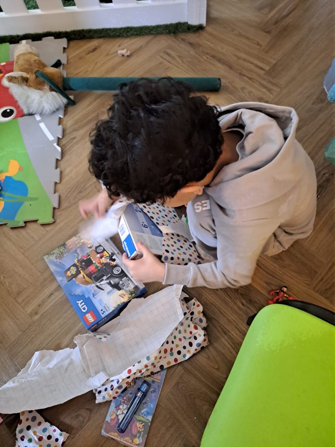 A child sits on the floor tearing the wrapping paper from a Lego set.