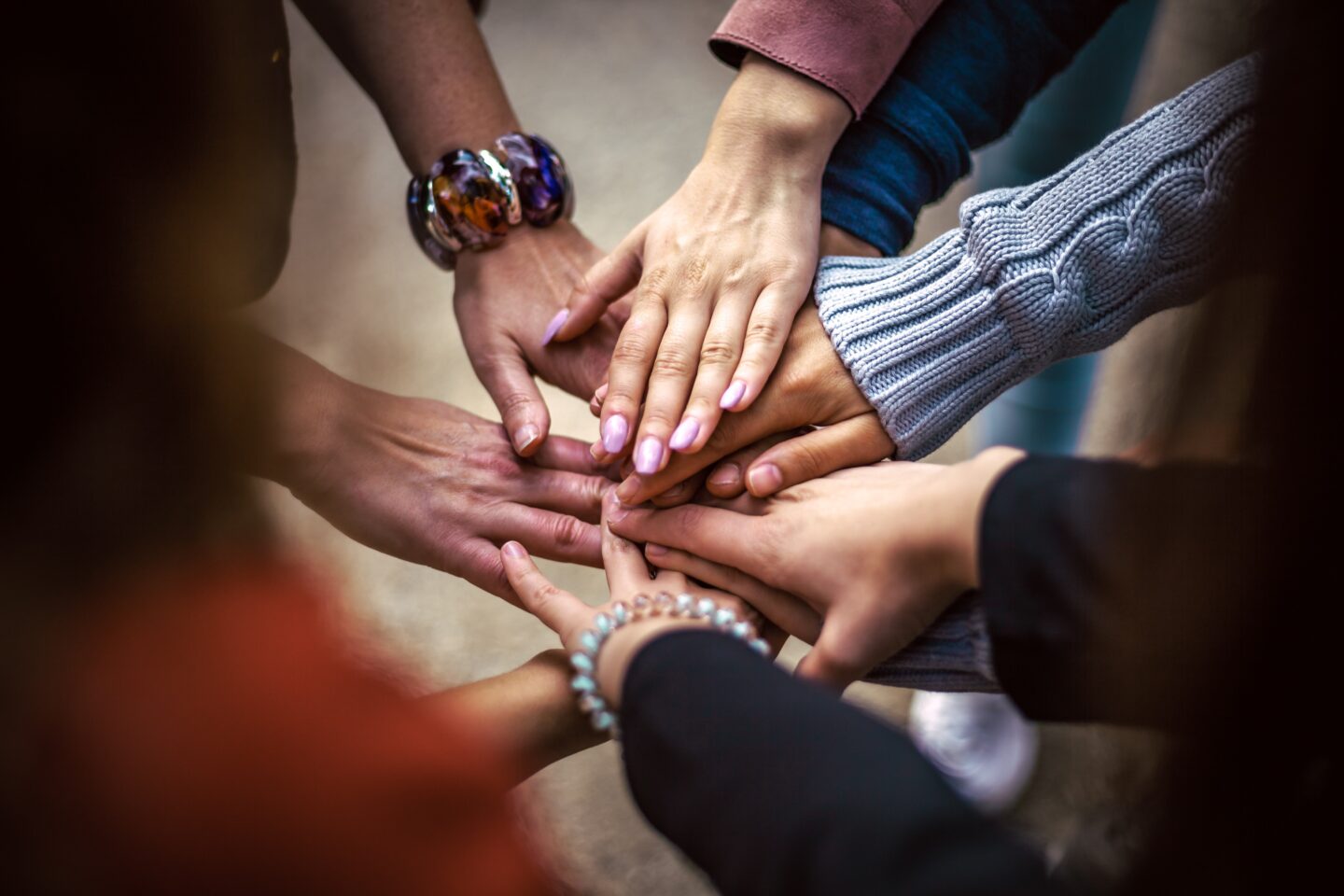 A group of hands stacked together, showcasing diverse skin tones and accessories, symbolizing unity and collaboration.