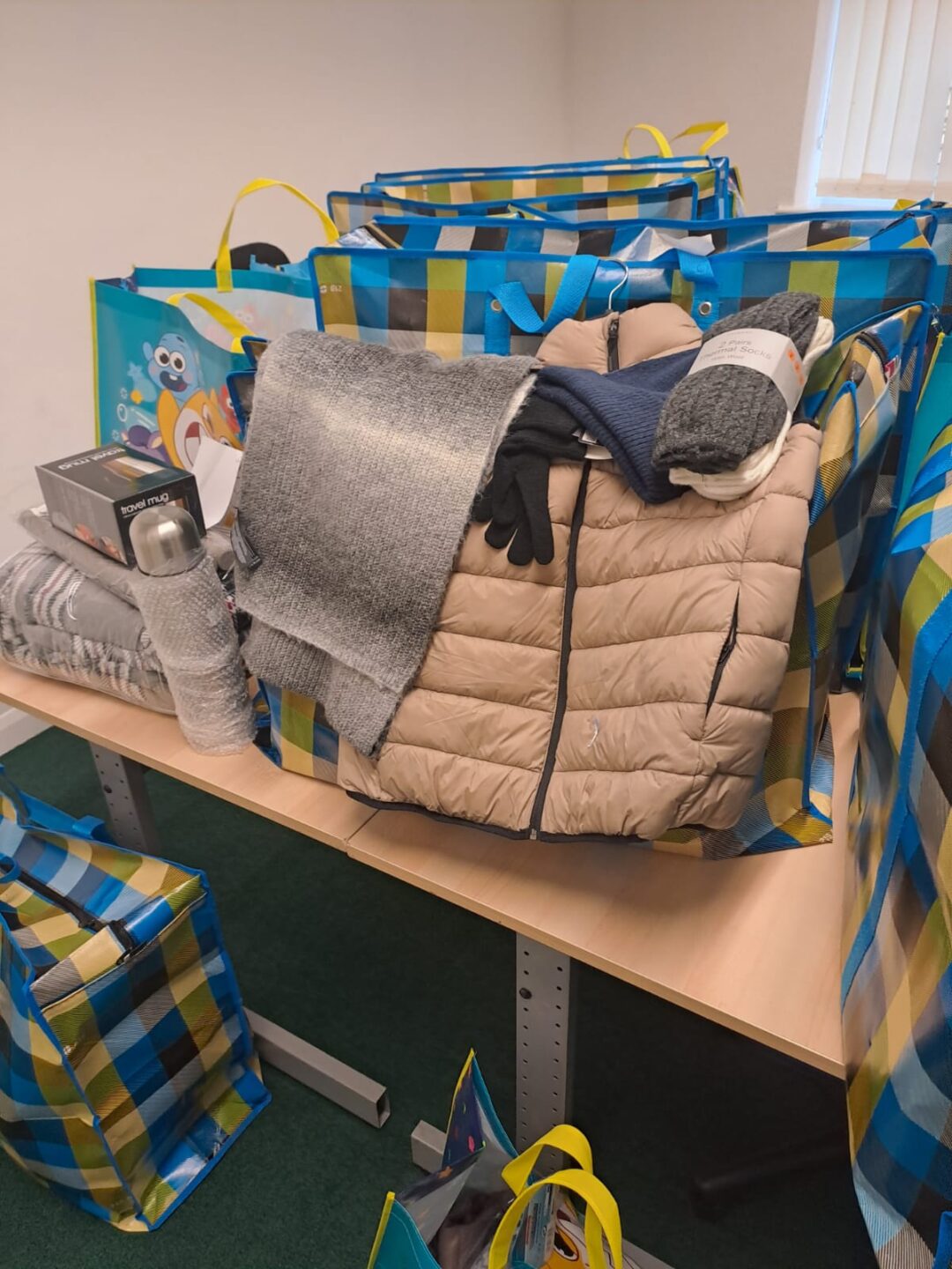 Several large bags are filled with winter clothing items, including a puffer jacket, gloves, and blankets.