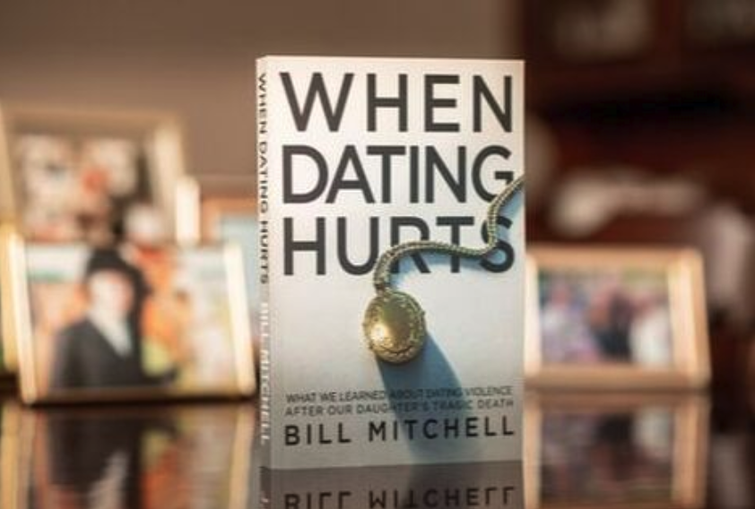 A book titled "When Dating Hurts" by Bill Mitchell, with a gold locket on the cover, is displayed in front of blurred family photos.
