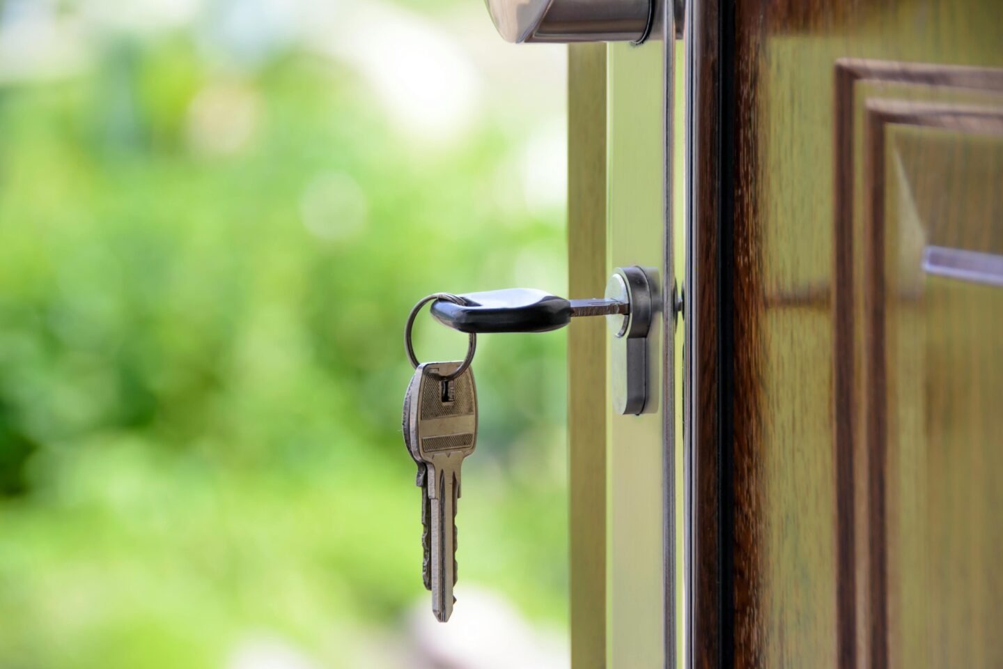 A key is inserted in a door lock, with the keychain visible, set against a blurred green background.